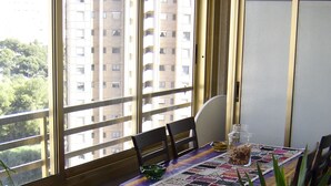 A dining area with a table set for two, a potted plant, and a view of a tall building through large windows. - BALI-BENIDORM HOTEL FRONT APARTMENT (Finestrat)