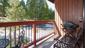 A balcony with a grill, chairs, and a view of trees. - (A204) Loft Condominiums (Yosemite National Park)