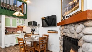 A cozy kitchen with a stone fireplace, a dining table with chairs, and a flat-screen TV mounted on the wall. - (A204) Loft Condominiums (Yosemite National Park)
