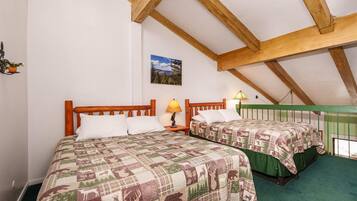 A bedroom with two beds, wooden headboards, a green railing, and a painting on the wall.