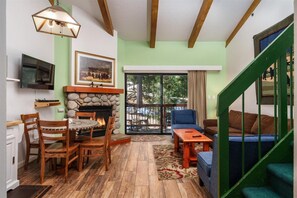 A cozy living room with a fireplace, wooden furniture, and a staircase with green railings. - (A204) Loft Condominiums (Yosemite National Park)