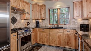 Eine moderne Küche mit Holzschränken, Edelstahlgeräten und einem großen Fenster mit Blick auf den Wald.