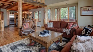 Ein geräumiges Wohnzimmer mit Holzbalkendecke, einer großen Couch, einem Couchtisch und Blick ins Freie durch große Fenster.