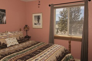 Une chambre à coucher avec un lit, une table de chevet, une lampe, un tableau encadré et une fenêtre avec des rideaux.