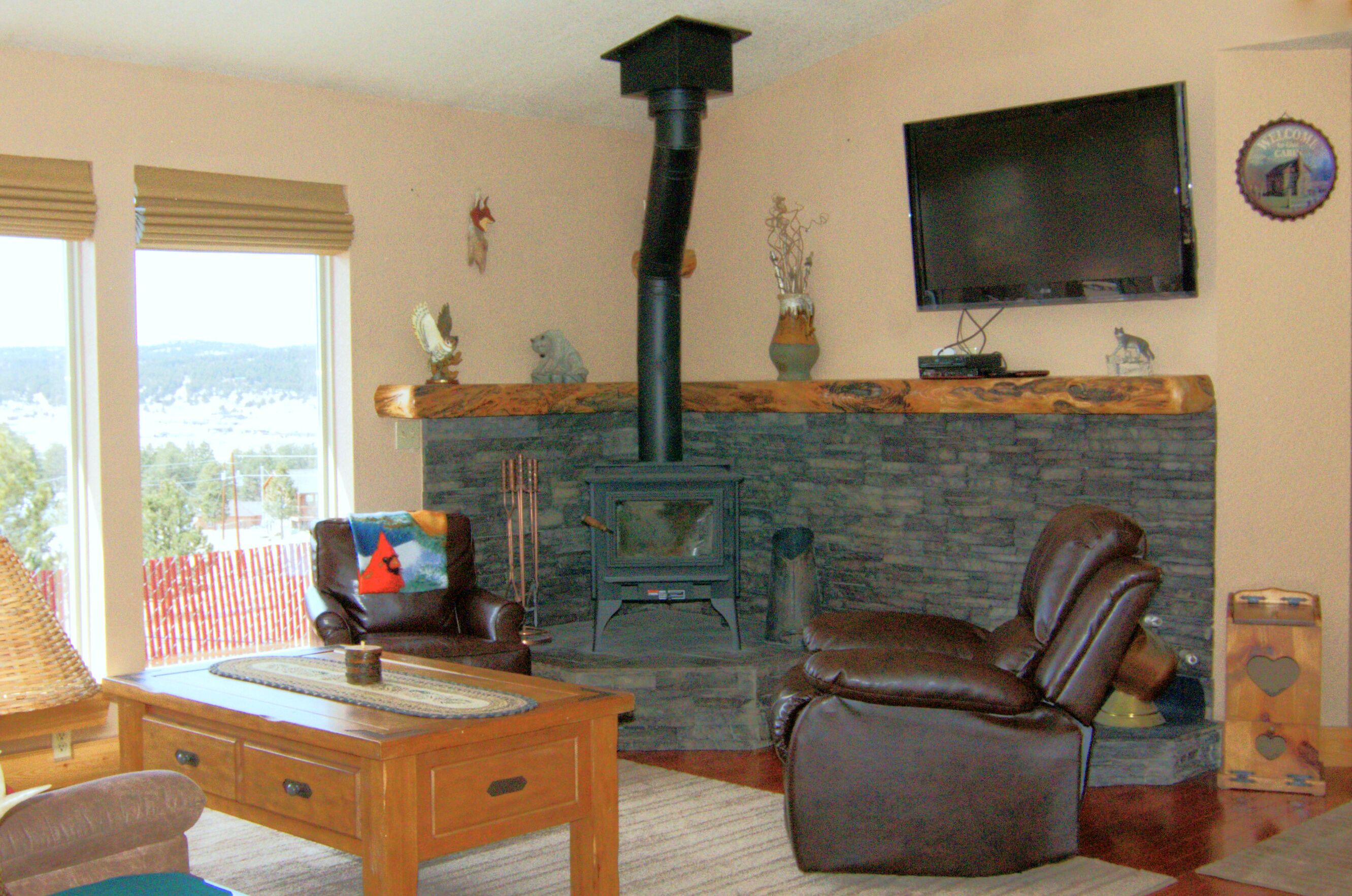 A living room with a stone fireplace, leather chairs, a wooden coffee table, and a television mounted on the wall.