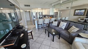 A modern living room with a grey sofa, a coffee table, and a TV on a black stand. - Sunset Jetty View! Enjoy one free beach chair set up and umbrella each day! (Destin)