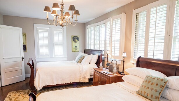 A bedroom with two beds, a chandelier, a nightstand, and a window with shutters. - Guest House of Kentucky (2 Queens - 1st Floor) (Lancaster)