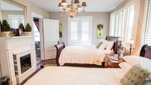 A hotel room with two beds, a fireplace, a chandelier, and a large window with shutters. - Guest House of Kentucky (2 Queens - 1st Floor) (Lancaster)