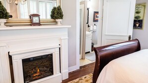 A bedroom with a fireplace, a bed, a wooden bench, a mirror, and a door leading to a bathroom. - Guest House of Kentucky (2 Queens - 1st Floor) (Lancaster)