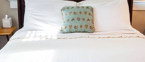 Una cama bien hecha con sábanas blancas y una almohada decorativa con estampado de concha.