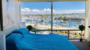 Ein Schlafzimmer mit großem Fenster mit Blick auf einen Yachthafen und die Skyline der Stadt.