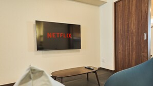 A room with a television mounted on the wall displaying the Netflix logo, a small table with a remote control, and two sofas. - TOKYO Condominiun HOTEL ASAKUSA EIGHT (Tokyo)