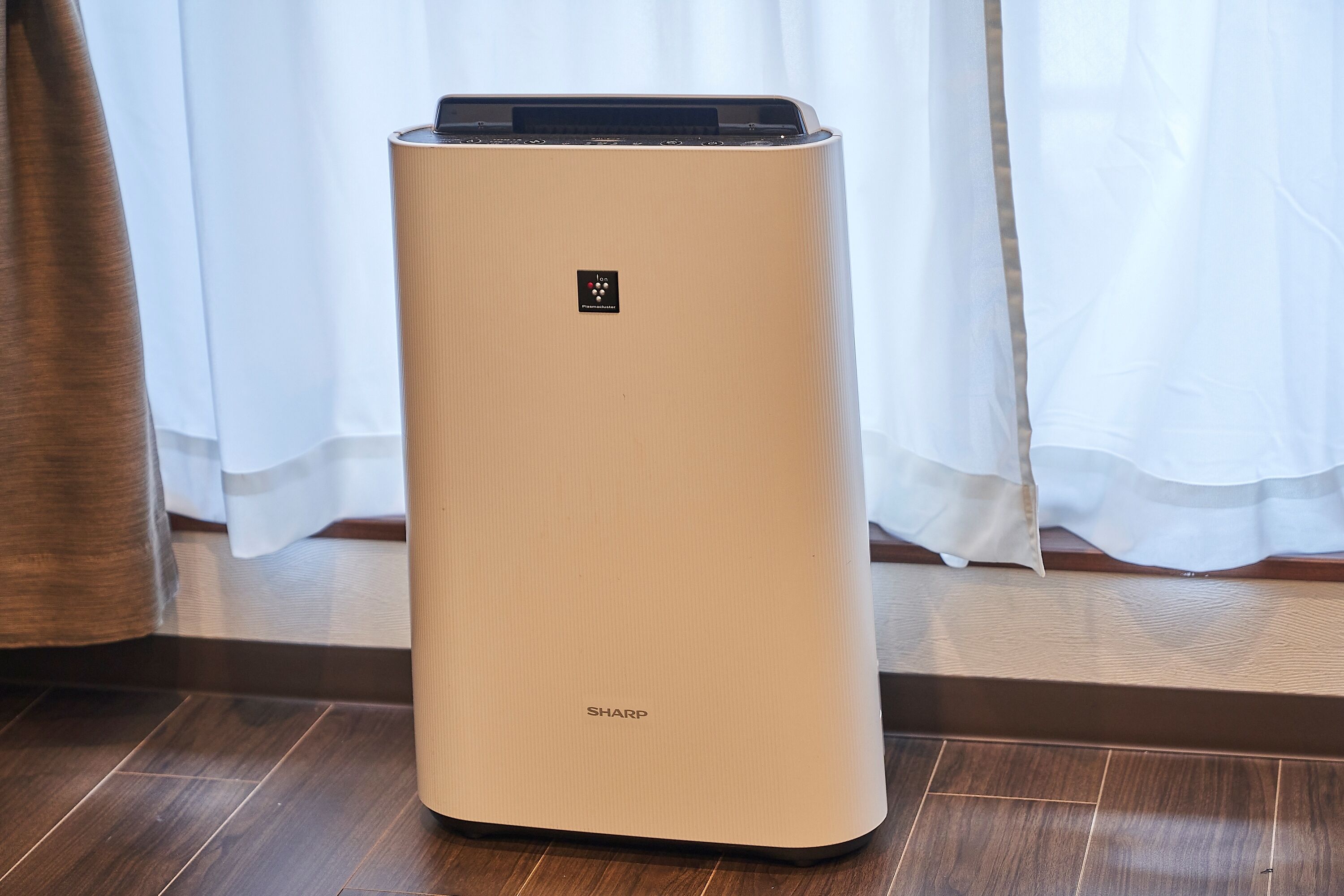 A beige air purifier with the brand name 'SHARP' on a wooden floor.