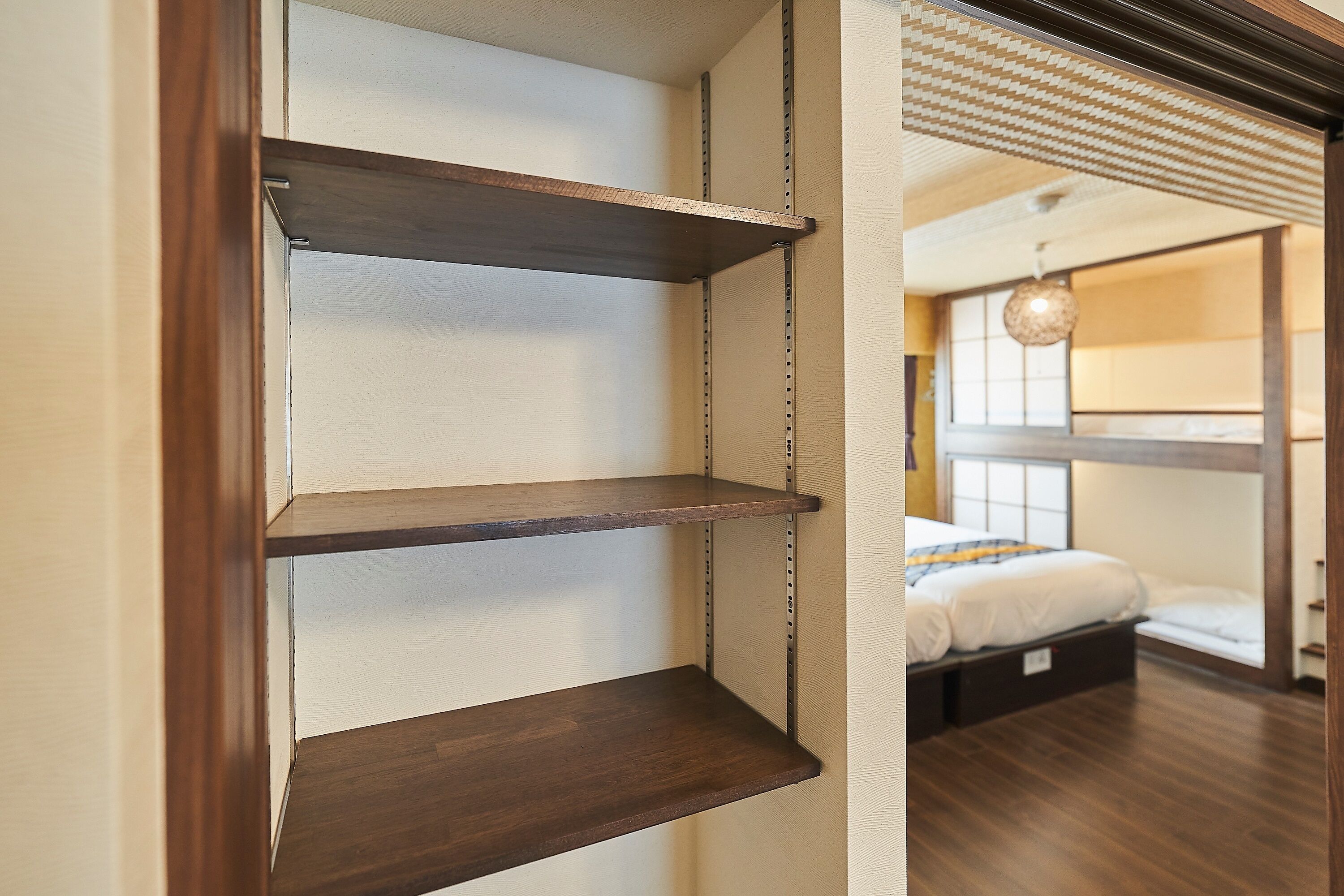 A room with a wooden shelf unit against a wall, a bed with a white mattress and a striped blanket, and a hanging light fixture.