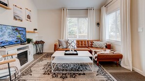 A living room with a sofa, coffee table, TV, fireplace, and a large window with curtains.