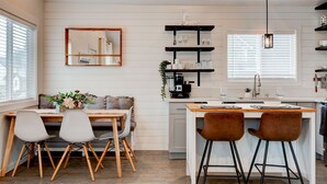 A modern kitchen with white cabinetry, a dining area with a wooden table and chairs, and a bar area with stools.