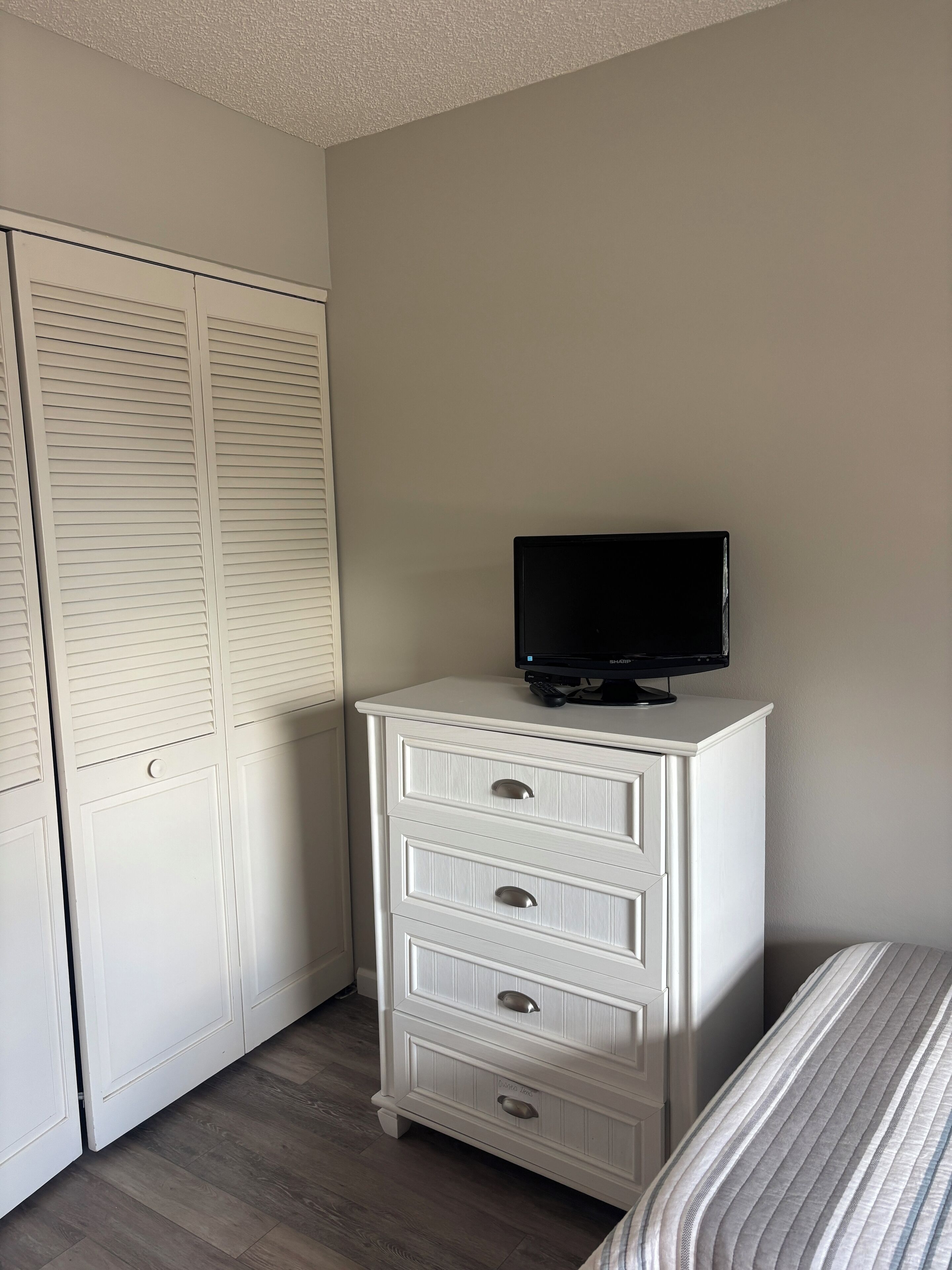 A bedroom with a white dresser, a television on top, and a striped bedspread.