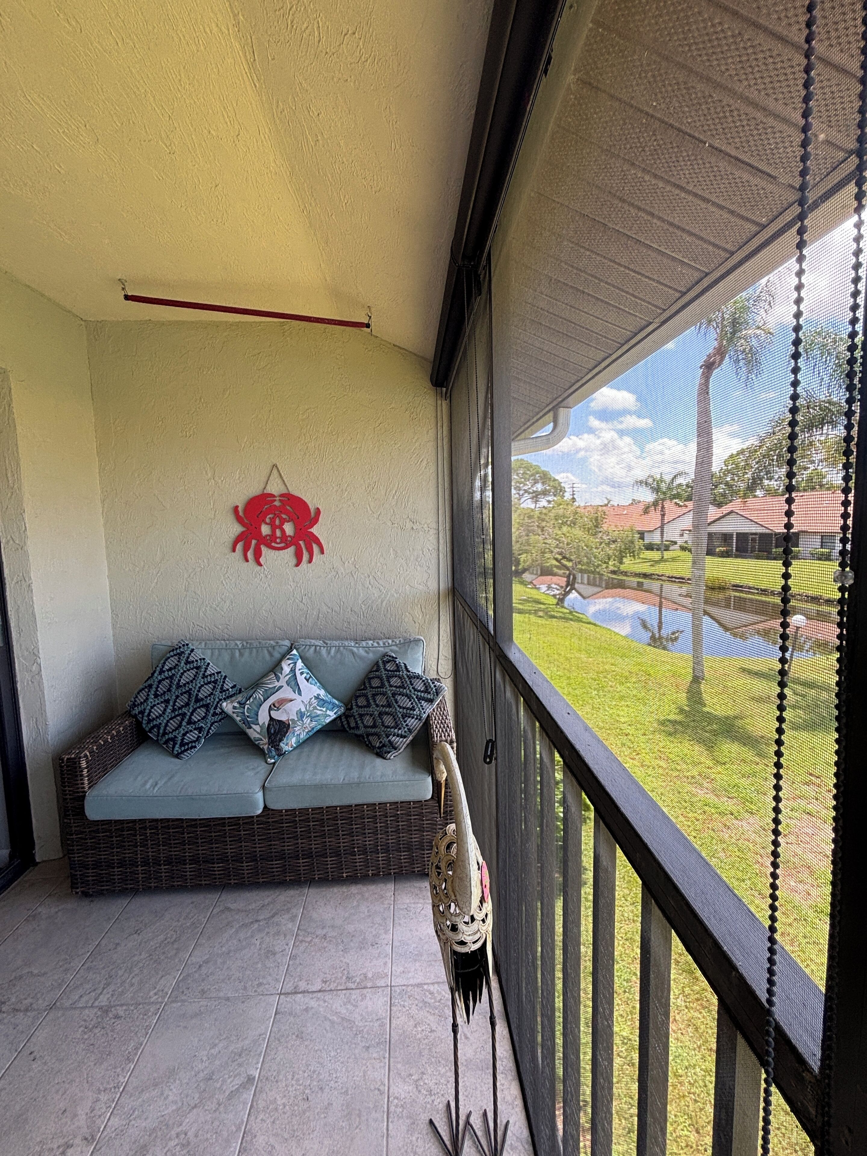 Ein Balkon mit einer Korbus-Sofasitzgruppe, einem dekorativen Wandbild mit Krebsen sowie Blick auf eine grüne Rasenfläche und Gebäude.
