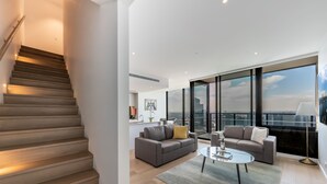 A modern apartment with a staircase, a living area with a sofa and coffee table, and large windows offering a city view. - Melbourne Private Apartments - Collins Wharf Waterfront, Docklands (Docklands)