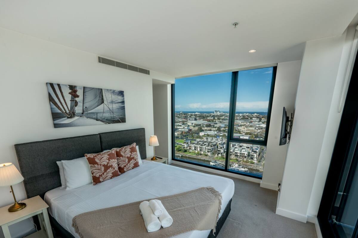 Een moderne hotelkamer met een groot bed, uitzicht over de stad en een schilderij aan de muur.