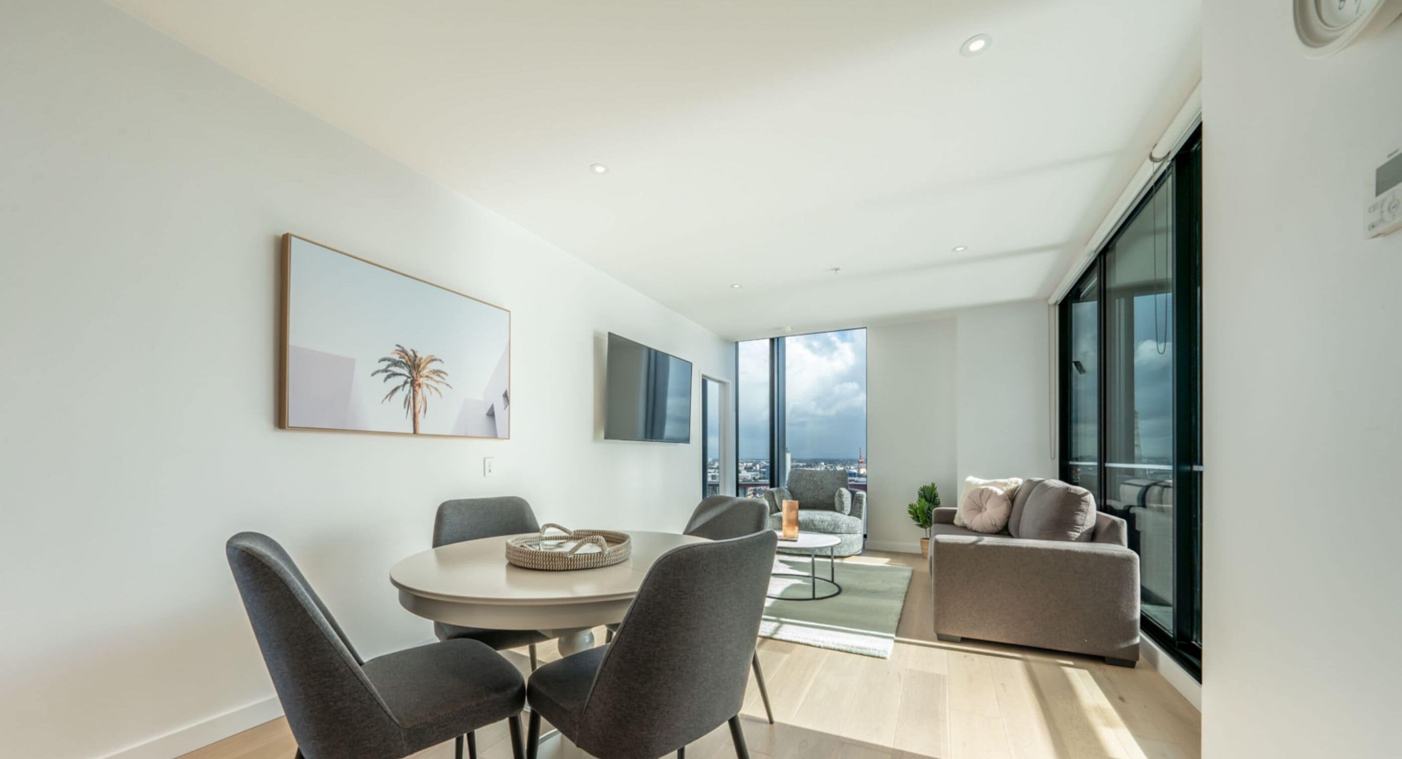 A modern living room with a dining area, large windows, and a view of the city.
