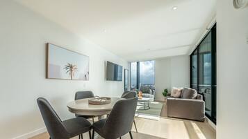 A modern living room with a dining area, large windows, and a view of the city.