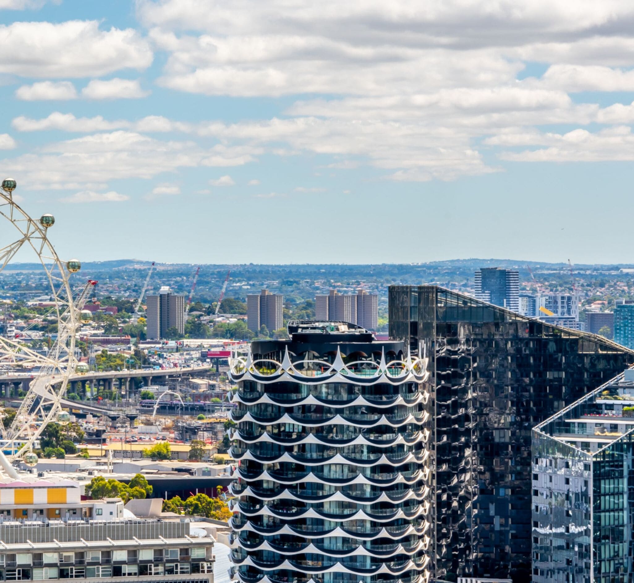 Un paysage urbain moderne avec des bâtiments à l’architecture remarquable, notamment une structure incurvée dotée d’une façade ondulée et une grande roue en arrière-plan.