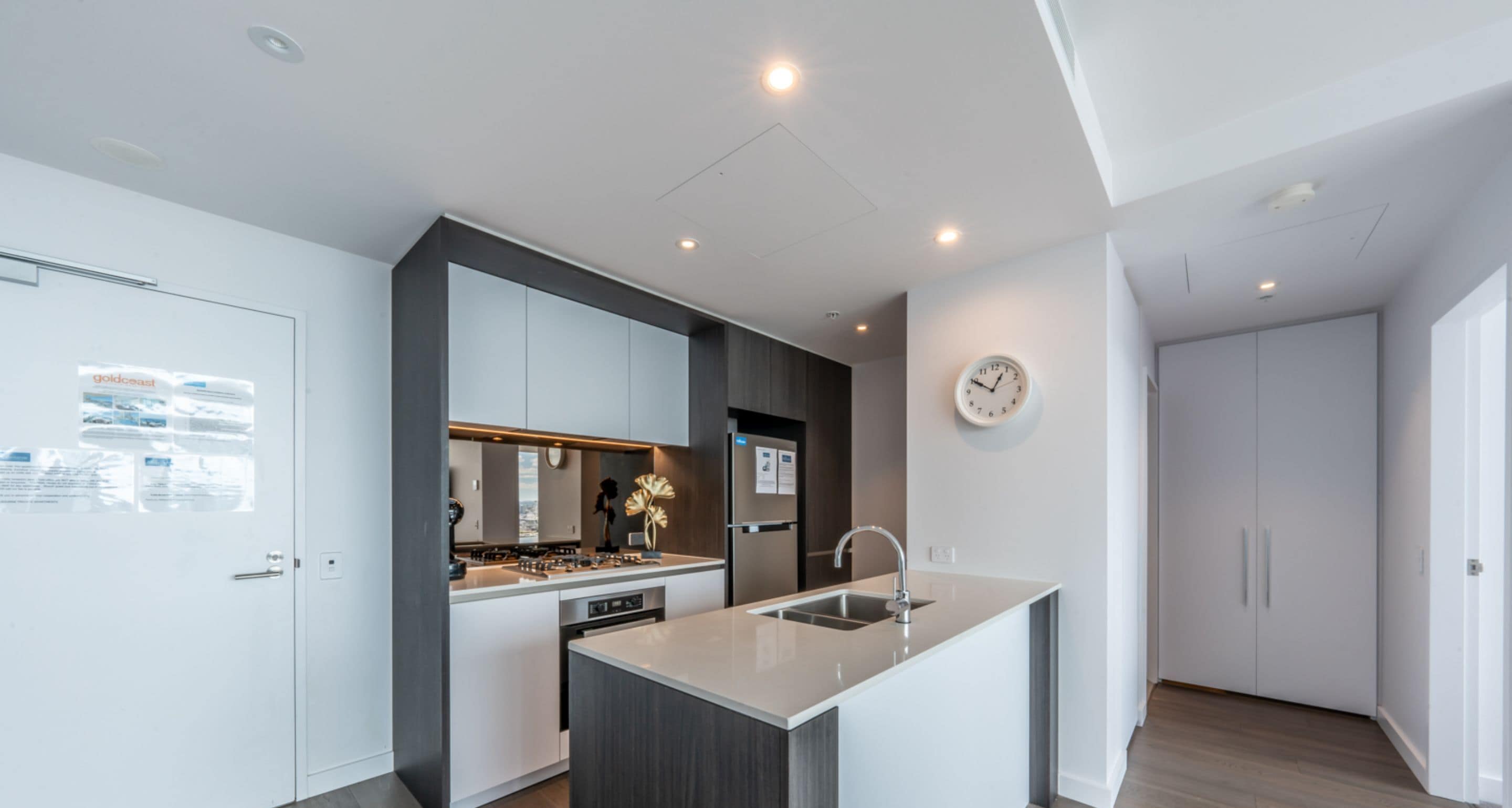 A modern kitchen with a central island, built-in appliances, and a clock on the wall.