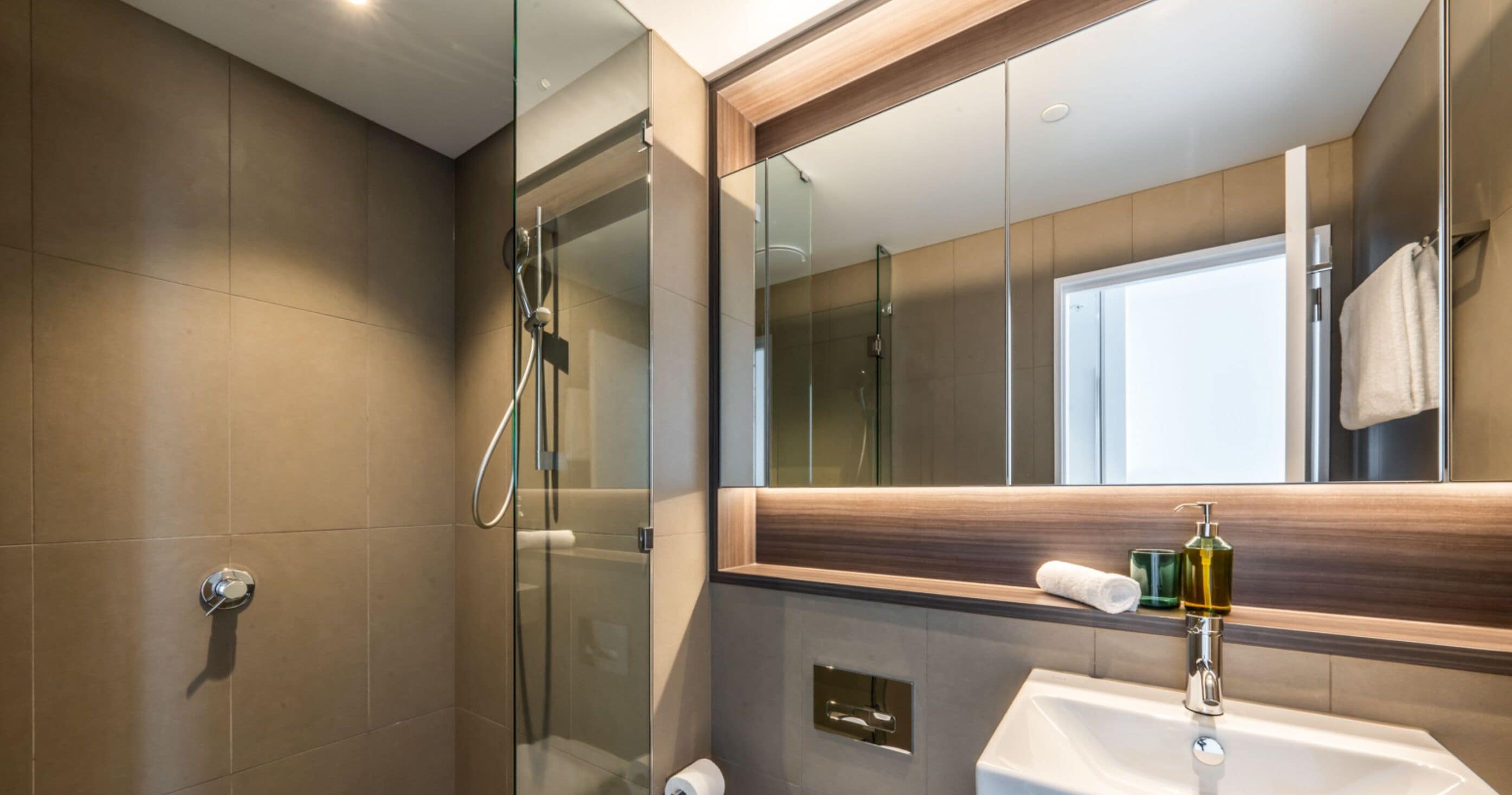 A modern bathroom with a glass shower enclosure, a sink with a mirror above, and a towel hanging on the wall.