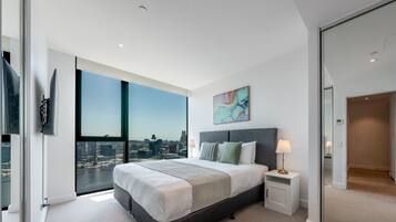 Une chambre moderne avec un grand lit, une table de chevet, une lampe et une vue sur la ville grâce à de grandes fenêtres du sol au plafond.