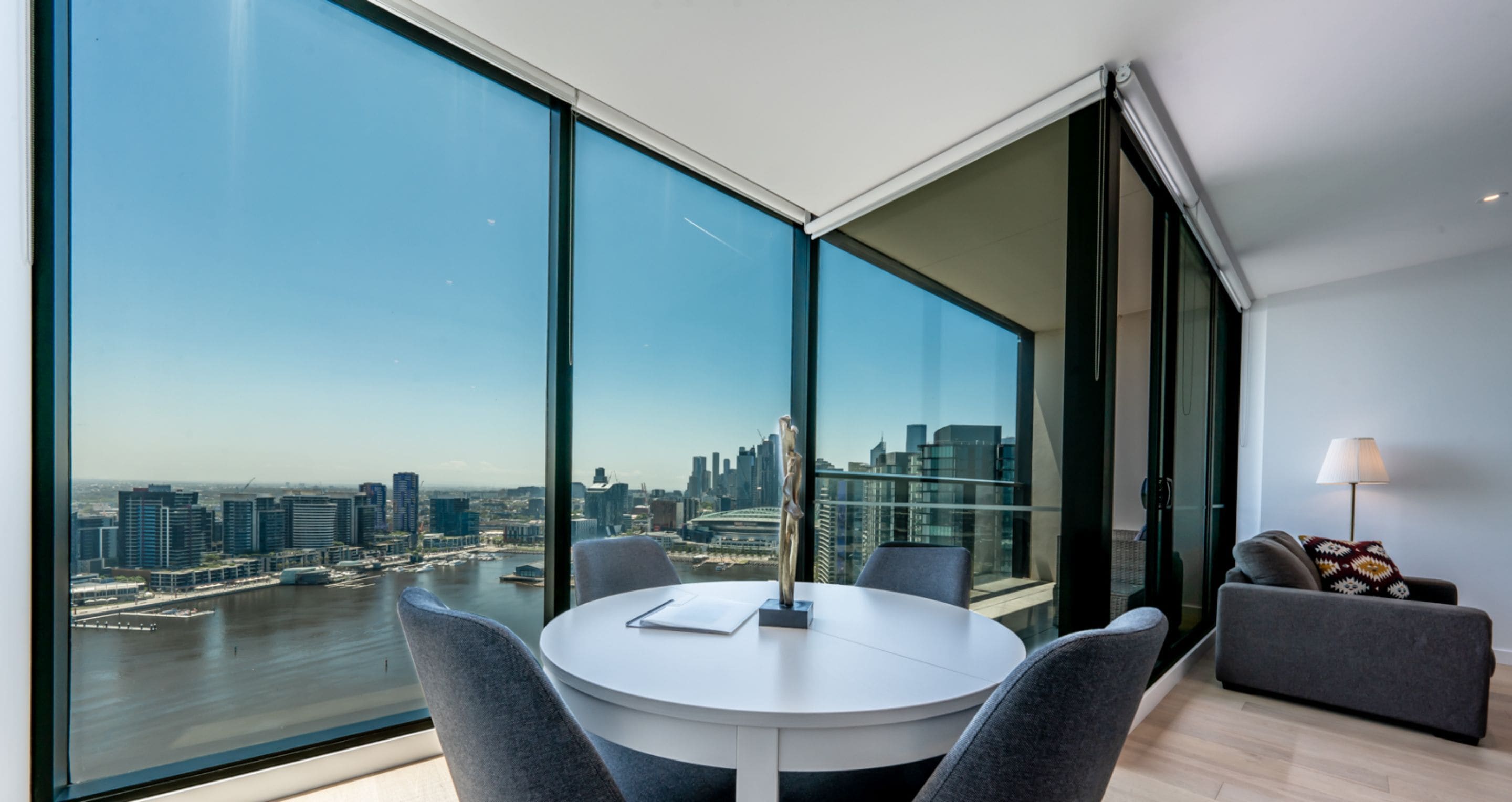 Een moderne kamer met een groot raam met uitzicht op de stad, een ronde tafel met stoelen en een bank.