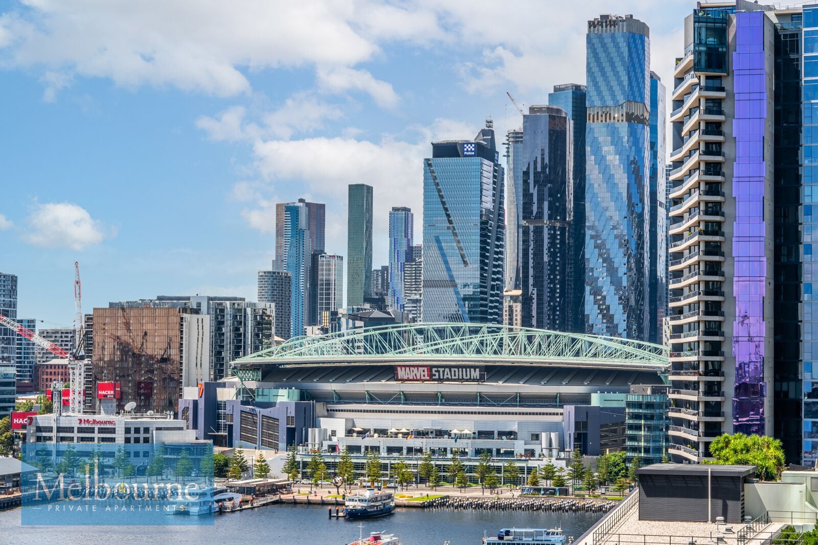 A cityscape with modern high-rise buildings, a prominent stadium, and a waterfront area.