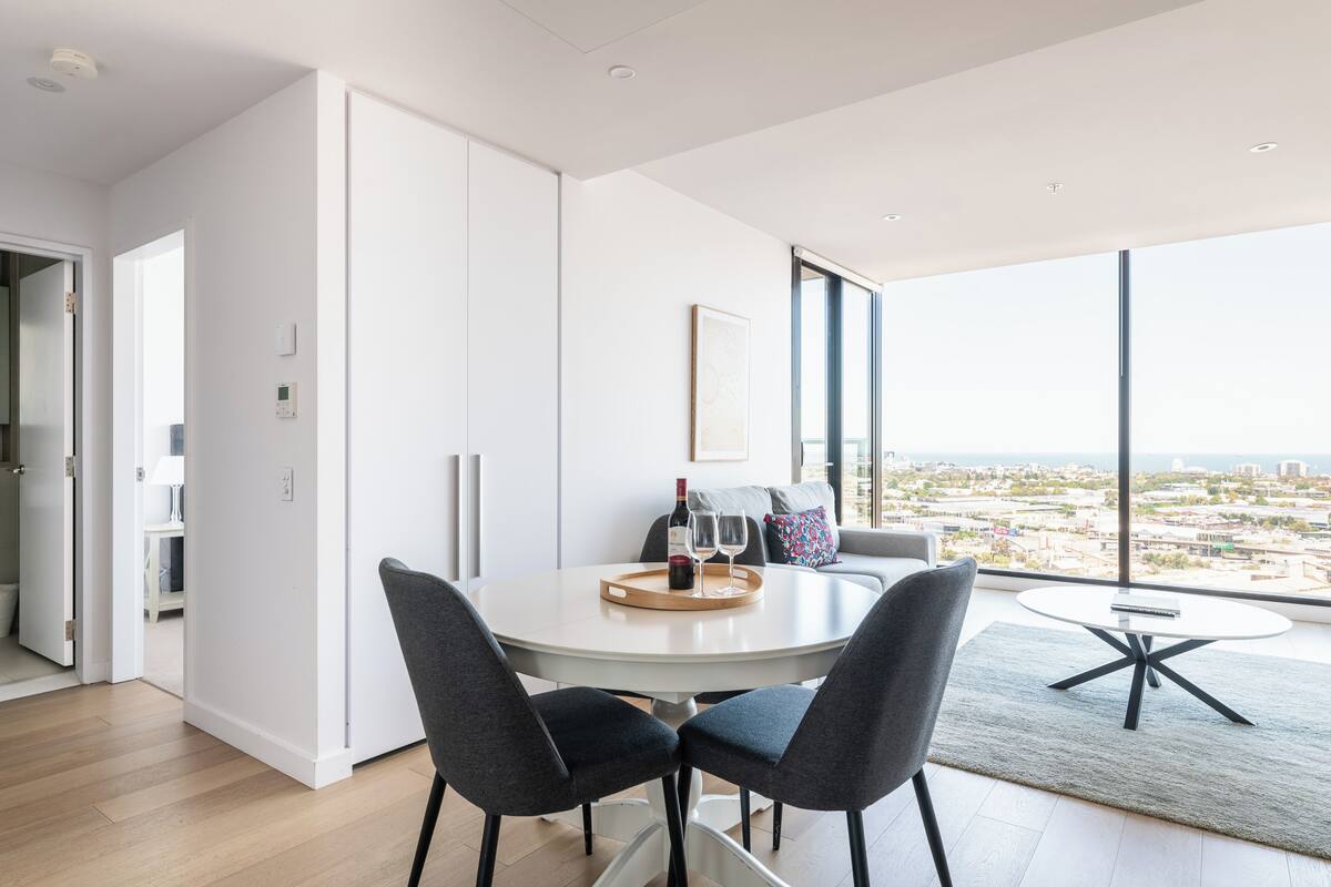 Een moderne eetruimte met een ronde tafel, twee stoelen en uitzicht op de stad door grote ramen.