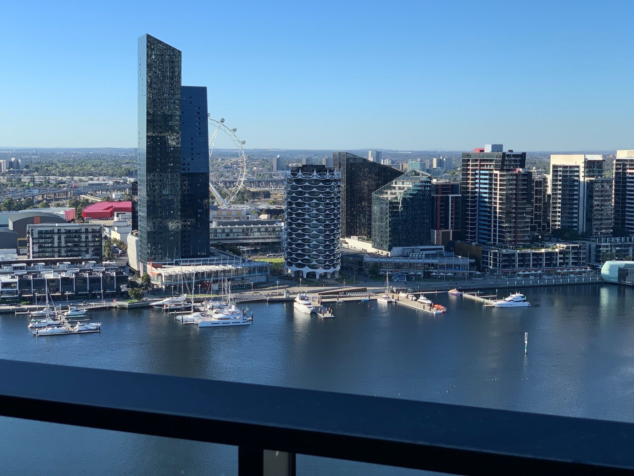 A city skyline with modern buildings, a marina with boats, and a clear blue sky.