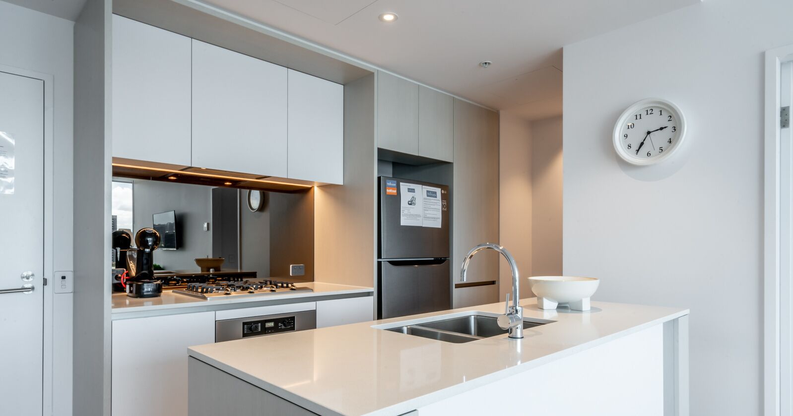 A modern kitchen with white cabinetry, stainless steel appliances, a built-in oven, and a sink with a faucet.