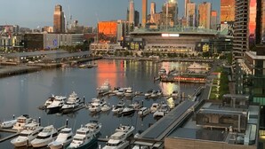 A marina with boats docked, a city skyline in the background, and a modern building with a unique roof structure. - Melbourne Private Apartments - Collins Wharf Waterfront, Docklands (Docklands)