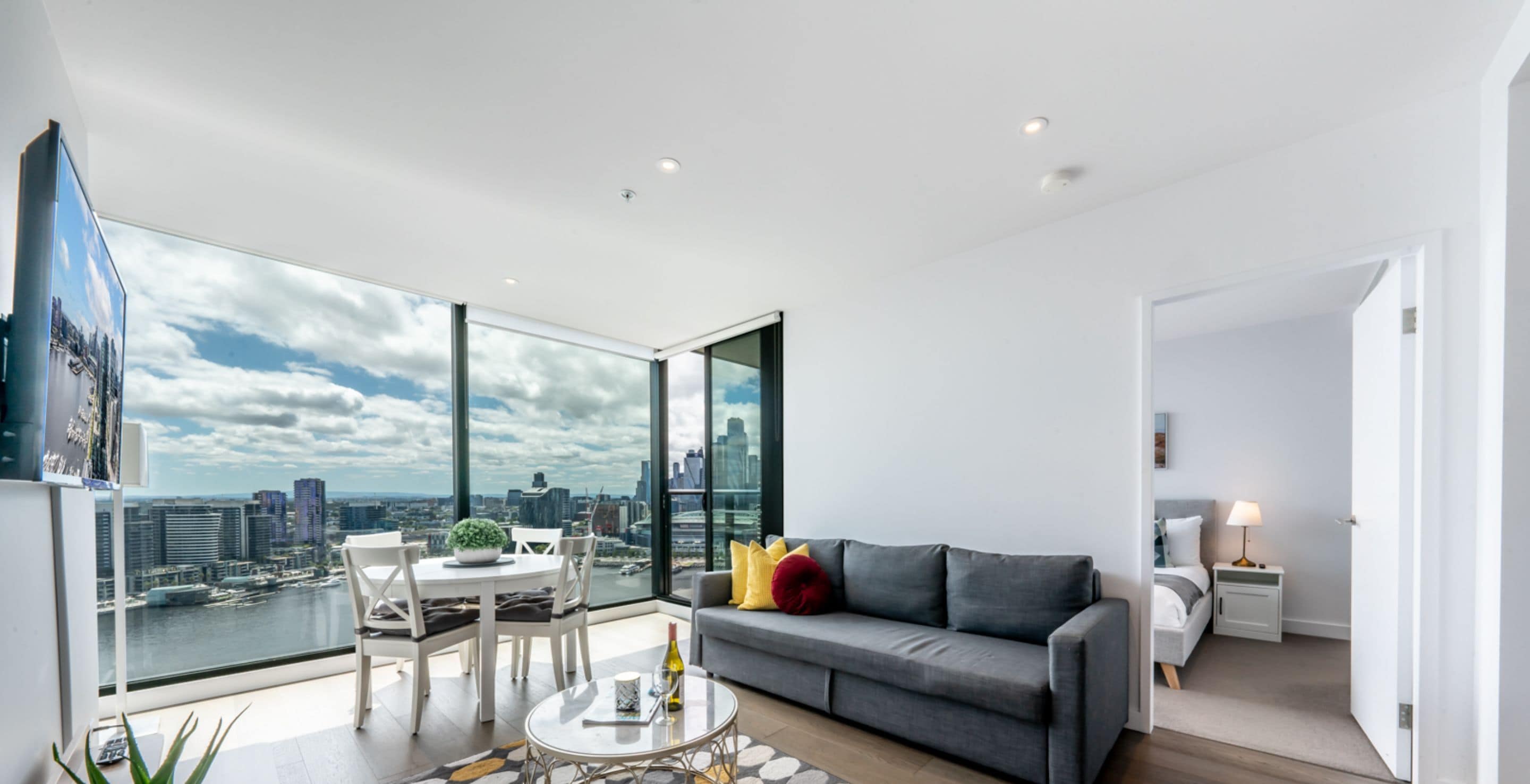 Un salon moderne avec vue sur la ville, un canapé gris, une table à manger et une lampe blanche.