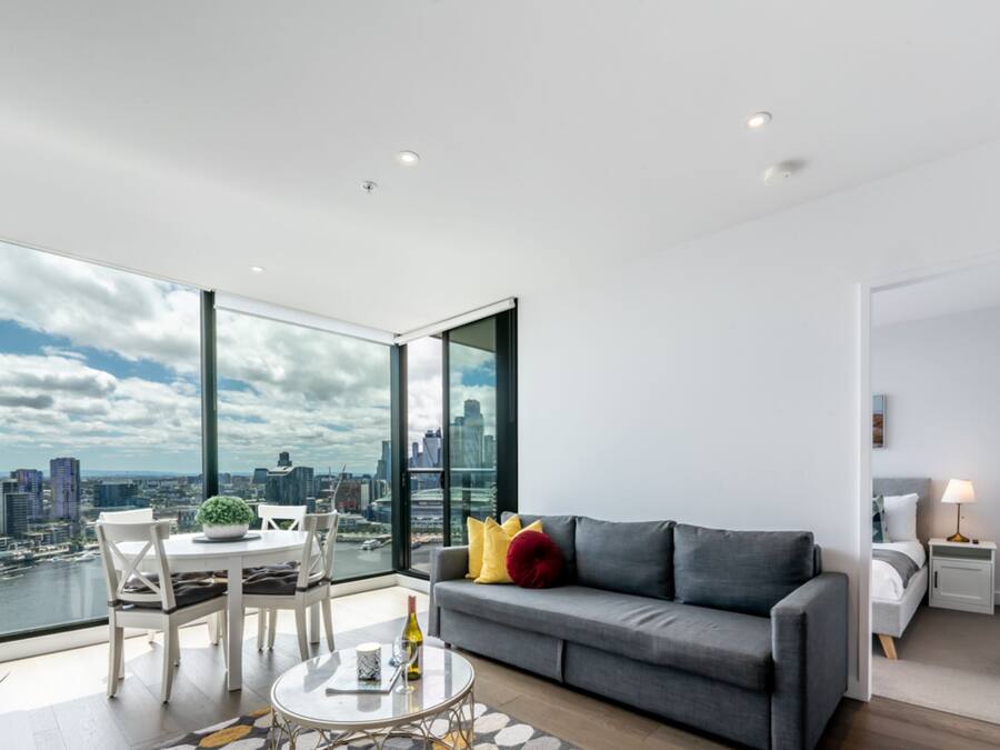 Un salon moderne avec vue sur la ville, un canapé gris, une table à manger et une lampe blanche.