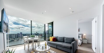 Una sala de estar moderna con vista a la ciudad, un sofá gris, una mesa de comedor y una lámpara blanca.