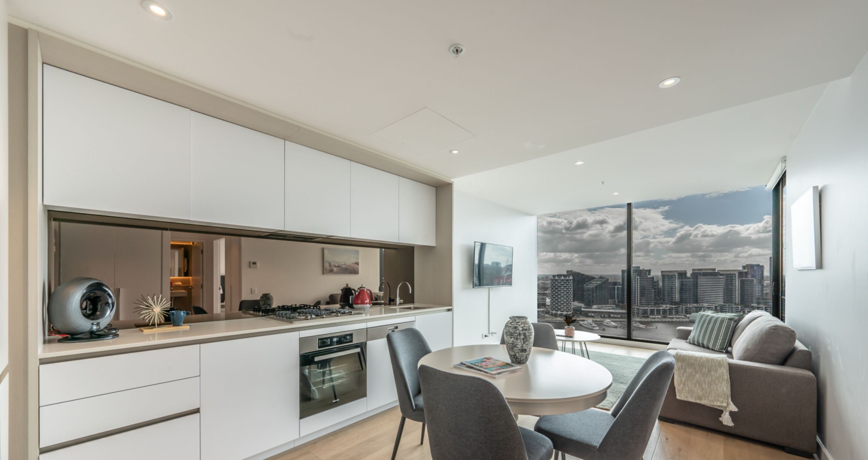 A modern kitchen with a dining area and a large window offering a city view.