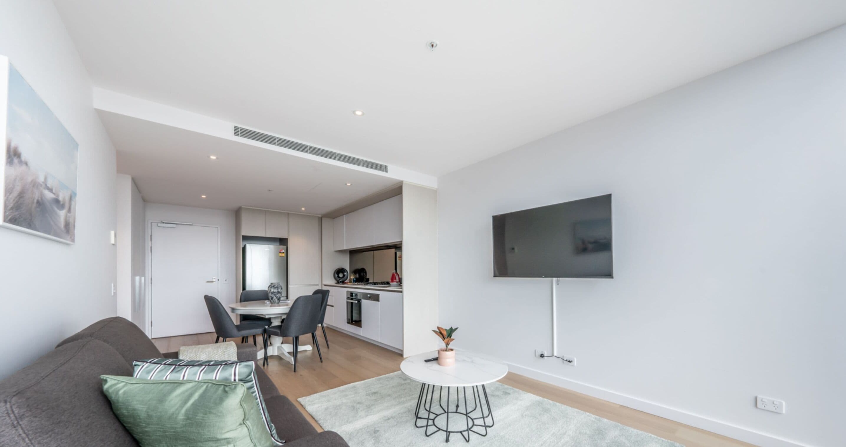 Un salon moderne avec un canapé gris, une petite table ronde et un téléviseur à écran plat fixé au mur.