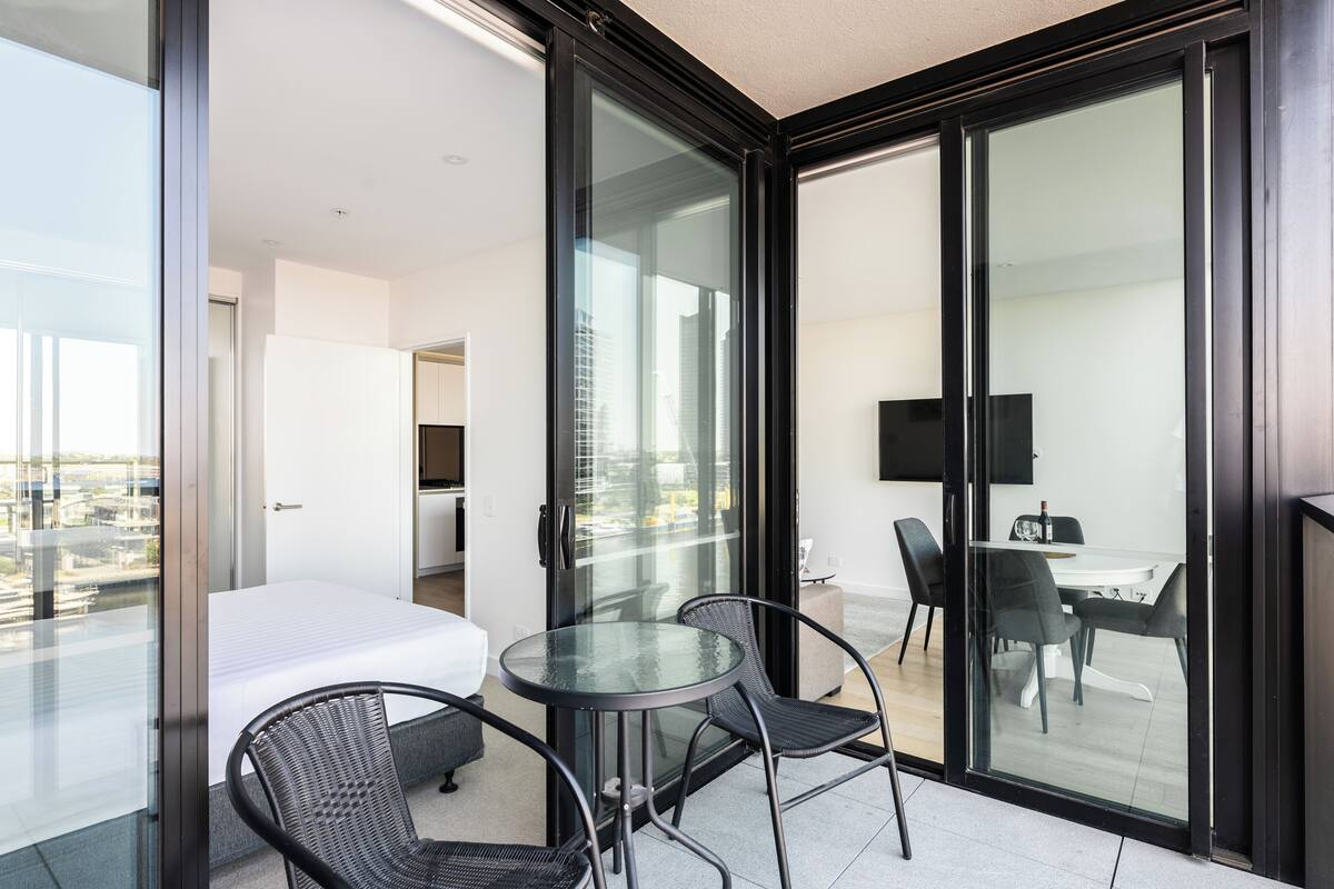 Een moderne hotelkamer met een balkon, een bed, een klein tafeltje met stoelen en een televisie in de aangrenzende ruimte.