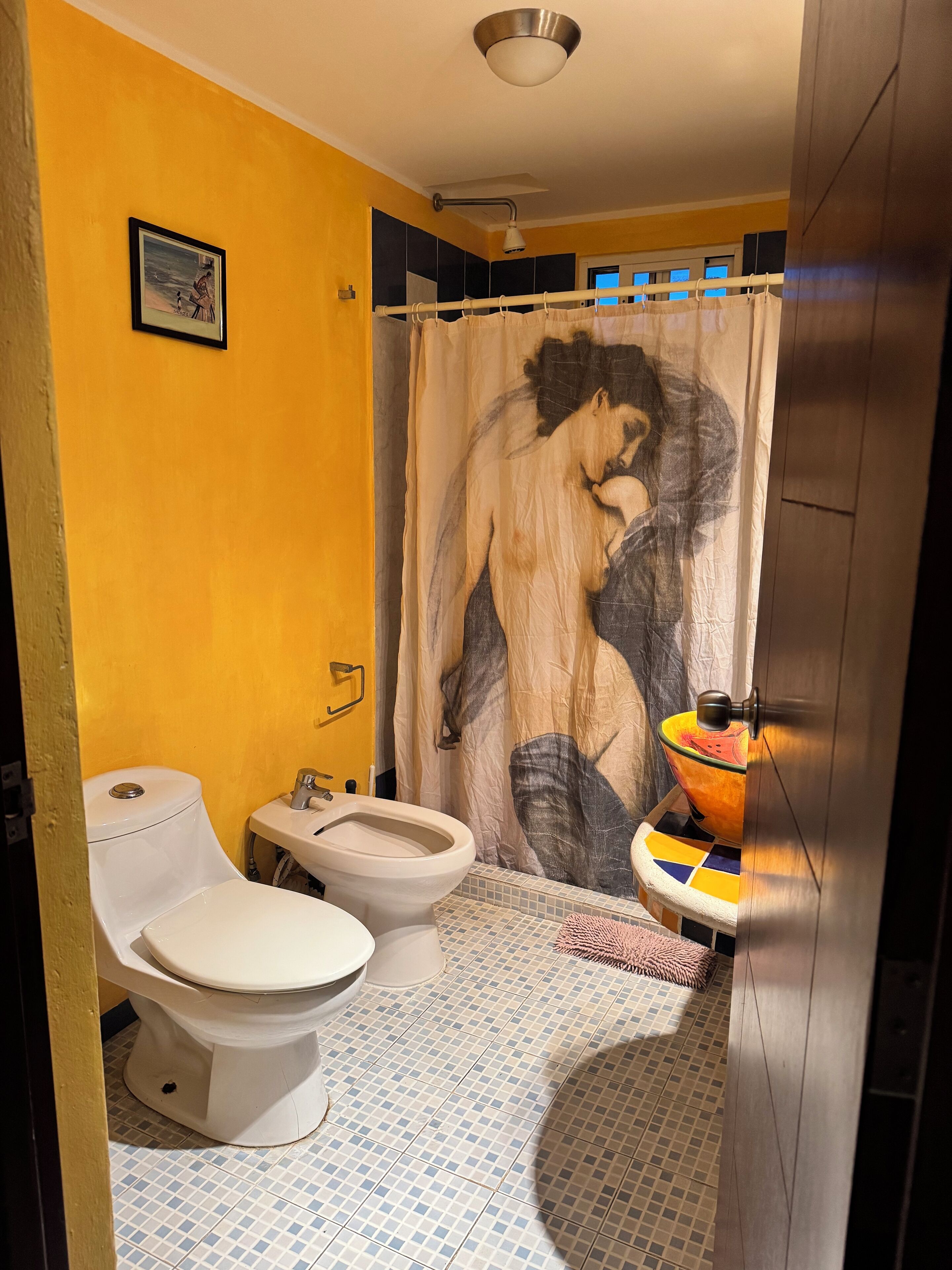 Een badkamer met twee toiletten, een wastafel, een douchegordijn met een grote afbeelding en een betegelde vloer.