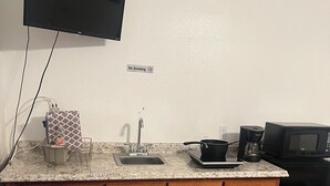 A kitchen with a granite countertop, wooden cabinets, a stainless steel sink, a microwave, and a coffee maker. - King Master Suite Studio (McAllen)