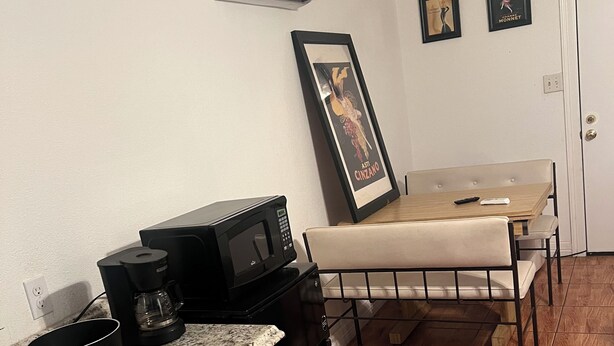 A compact kitchen with a microwave, coffee maker, and induction cooktop. A dining table with a bench is in the background. - King Master Suite Studio (McAllen)