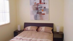 A bedroom with a bed, two nightstands, and a wall-mounted abstract painting. - Emada Venus Bay - a stone's throw from cafes and shops inVenus Bay (Venus Bay)
