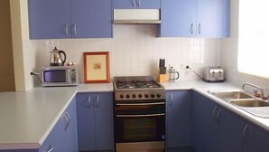 A kitchen with blue cabinets, a microwave, a gas stove, and a toaster. - Emada Venus Bay - a stone's throw from cafes and shops inVenus Bay (Venus Bay)