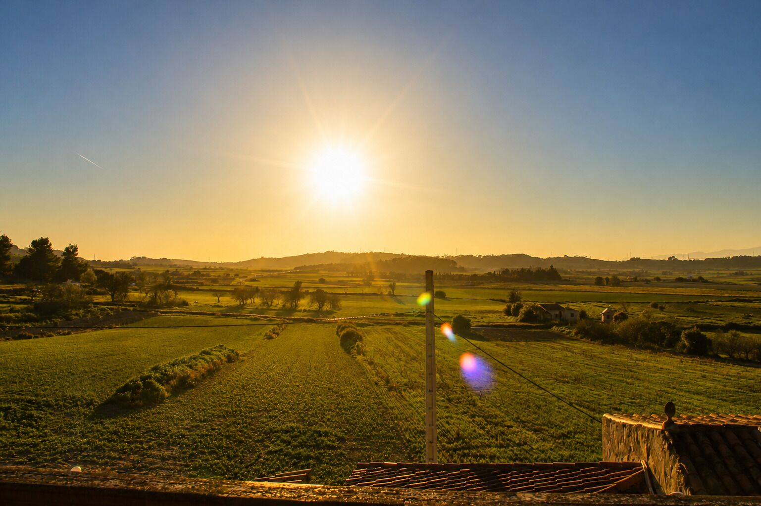 A rural landscape with fields, a wooden fence, and a distant hill.