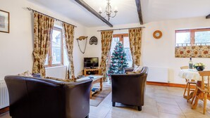 Un salon avec deux canapés en cuir, un téléviseur, un sapin de Noël et un coin repas comprenant une table et des chaises.