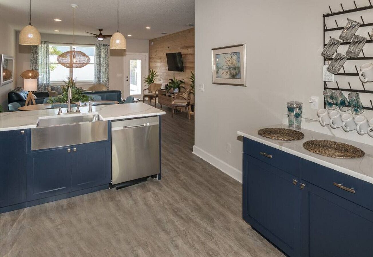 Een moderne keuken met een centraal eiland, blauwe kastjes, en een eethoek met een houten tafel en stoelen.
